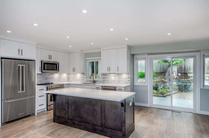 Modern kitchen renovation with white cabinets, large island, and patio doors